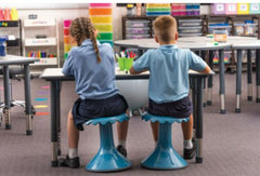 This is an image o9f 2 school children sitting on blue wriggle stools.