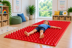 A wide, textured sensory walkway mat with a child lying on their back in an inclusive sensory play and therapy room.