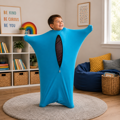 A child wearing a bright blue full-body elastic suit with a front zipper, standing on a round rug in a cozy, well-lit room with bookshelves and a beanbag.