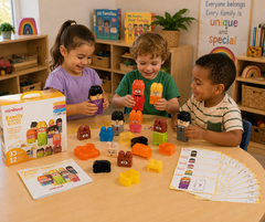 Three children playing with Miniland Family Blocks in a bright, colorful preschool classroom. The children are holding colorful building blocks, with the product box, instruction booklet, and sorting cards spread out on the wooden table in the foreground.