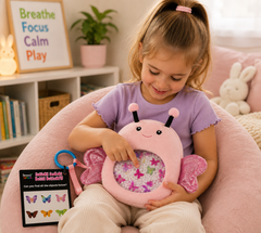 A young girl sits in a pink armchair, interacting with a butterfly-shaped sensory toy. The toy has a pink outer body with glittery pink wings and a clear center filled with colorful butterfly-shaped pieces.