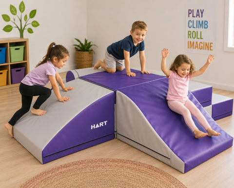 Three children climb, crawl and slide across a purple and grey Sensory Tactile Obstacle Mountain in a bright play space, supporting gross motor skills, balance, coordination and active sensory play.