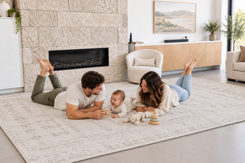 A couple playing toy time with their baby on a Sandstone memory foam mat with a distressed beige pattern in a modern living room.