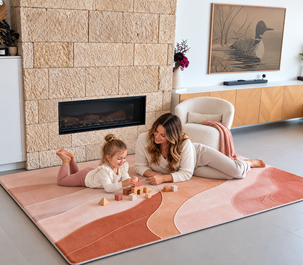 Clay Drift Designer Print Memory Foam Mat in warm blush, clay and terracotta tones, with a young child and adult enjoying floor play together in a contemporary living room.