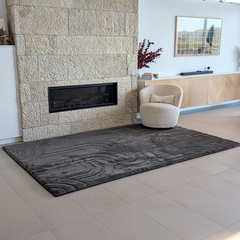 Charcoal coloured Cloud Haven Soft Touch Mat featuring a plush 35mm high-resilience foam surface and contemporary carved pattern placed in a living room next to stone fireplace and comfy chair