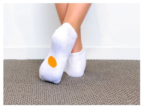 Legs of child wearing white Dot On A Sock ankle socks with orange dot on soles