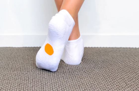 Legs of child wearing white Dot On A Sock ankle socks with orange dot on soles