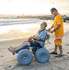 This is an image of the Sandcruiser All Terrain Dune Buster Wheelchair. It shows a person laughing while sitting and watching the water at the beach. It is Blue and has two large WheelEEZ wheels on the front and two large WheelEEZ wheels on the back.