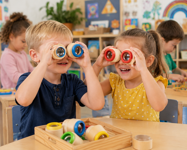 Children exploring colourful Hape Kaleidoscopes together in a bright preschool classroom.