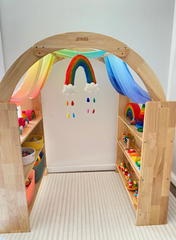 This is an image of the Wooden Interactive Play Stand and Retreat Den with colorful fabric and toys on the shelves. 
