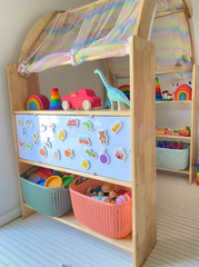 This is an image of the Wooden Interactive Play Stand and Retreat Den with colorful fabric and toys on the shelves. 