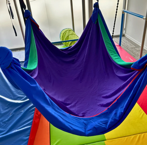 Colorful layered Lycra therapy hammock featuring a purple top layer with blue, green, and red layers beneath.