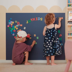 Two young children create on a navy coloured Magnetic Chalk Wall Decal used as a wall-mounted magnetic building and creative play surface in a children's playroom.