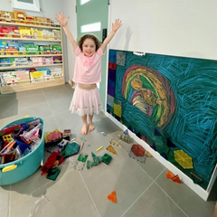 Child creating artwork on a forest coloured magnetic chalk wall decal, combining chalk drawing with colourful magnetic tiles in an early learning environment.