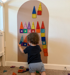 A young child arranges magnetic shapes on a cocoa coloured Magnetic Chalk Wall Archway that encourages hands-on exploration, construction skills and independent engagement.