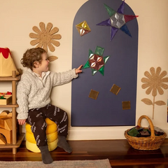 A young boy touches magnetic shapes stuck to a navy coloured Magnetic Chalk Wall Archway that supports creative exploration, visual-spatial skills and independent play.