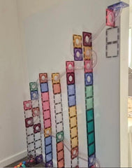 Colourful magnetic construction tiles and transparent ball-run components arranged vertically on a magnetic wall decal for interactive building and STEM activities.