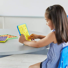 Young girl at a table traces the maze on a yellow Mindful Maze board