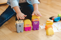 Child's hand shown playing with colorful toy figures on a wooden floor