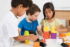 Three children of different nationalities playing with colorful building blocks at a table.