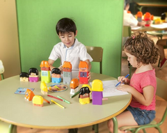 Two children playing with toy figures and coloring at a table in a classroom setting.