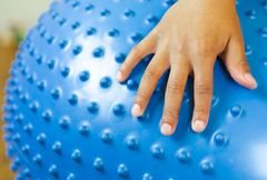 Close up of child's hand on the Inflatable Sensory Ball with Tactile Nubs peanut-shaped balance ball for flexible seating, occupational therapy, physiotherapy, classroom learning, NDIS support and core strength development.