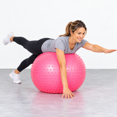 An adult is doing a side plank on a large pink spiky stability ball.