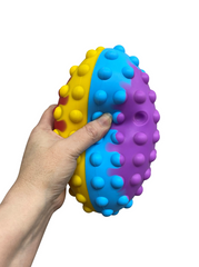 Hand squeezing the red, yellow, and blue coloured Pop It Ball Fidget with tactile pop bubbles for emotional regulation, fine motor development, occupational therapy, classroom focus, NDIS support and stress relief.