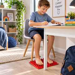 Acupressure sensory mat providing tactile foot stimulation for a child studying at home.