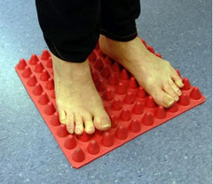 This is an image of someone standing on a Red Sensory Feedback Tactile Square Mat - for Autism and Sensory Regulation.