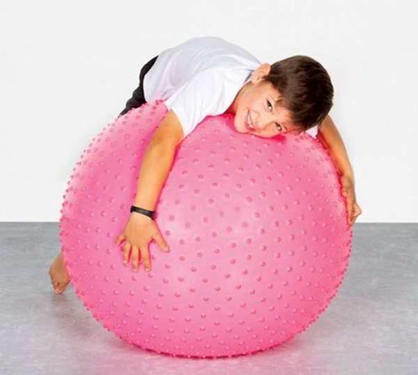 Child using a pink 65cm Spike Swiss Ball during a gross motor activity to develop balance and coordination.
