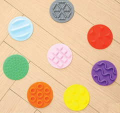 Close up of the 8 different textures of disc shaped "stones" in the Tactile Balance Stones & Beams 20 piece sensory balance set 