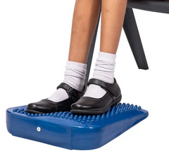 Blue coloured tactile foot and support wedge in use by young student placed under a classroom desk to support sensory regulation, focus and calm seated movement.