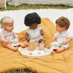 Toddler baby girl doll with hearing implant sitting up with two friends at a tea party