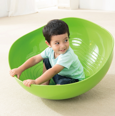 Child rocking and balancing in green WePlay Rocking Bowl for gross motor development