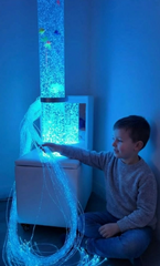 Image of a child playing with a fiber optic cable and a bubble tube on a mobile sofa podium, in a room bathed in soft blue light.