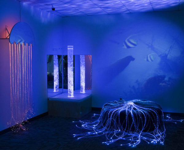 Image of a sensory room with bubble tube, sofa podium and fibre optic.