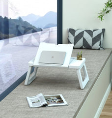 White laptop stand with a laptop on a gray floor, next to an open magazine and a plant.