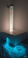 This is an image of a bubble tube with Fibre Optic lighting. It is sitting in a white podium and attached to the wall with a bracket.