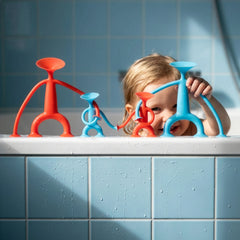 Image of a child in the bath, playing with red and blue Oogi figures by Moluk.