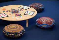 This is an amage of a round low table with 4 cushions on the floor with Indigenous art designs on them.