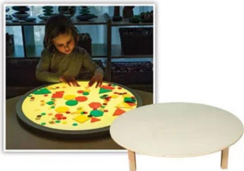 This is an image of a child using a round light panel with shapes on it. There is also a white table.