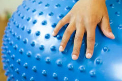 This is an image of a hand on a blue Therapy Inflatable Sensory Ball with Tactile Nubs that  is a peanut shape. It has tactile nubs all over it.
