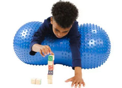 This is an image of a child lying on a blue Therapy Inflatable Sensory Ball with Tactile Nubs. It is a peanut shape. It has tactile nubs on the outside.