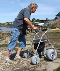 image of a all terrain rollator walker with beach wheels being used by a man walking across the rocks