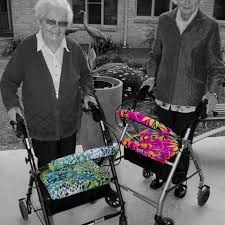 This is asn image of 2 older ladies with bright coloured covers on their wheelie walkers