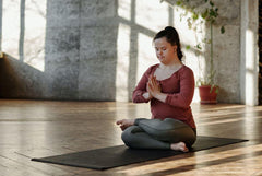 This is an image of a girl sitting on a black mat and practicing a yoga pose